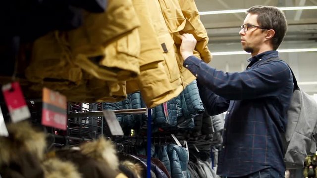 an adult man is in the store, a gentleman chooses a winter jacket for skiing, he looks at the clothes and checks its quality and heat resistance