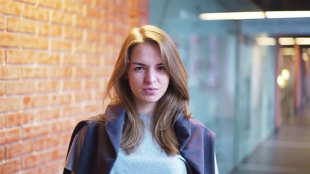 Calm and attractive young woman looking at camera and saying no as if disgusted by a request while standing in a building corridor with brick walls. Handheld slow motion medium shot