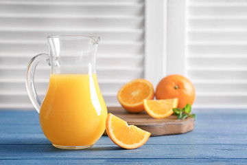 Glass jug of fresh orange juice with slice on wooden table