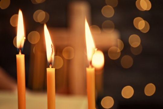 Burning candles and blurred cross on background
