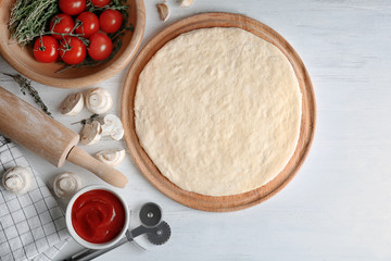 Raw dough for pizza with ingredients on kitchen table