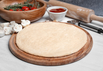 Raw dough for pizza with ingredients on kitchen table