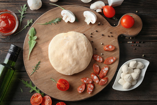 Raw dough for pizza with ingredients on kitchen table