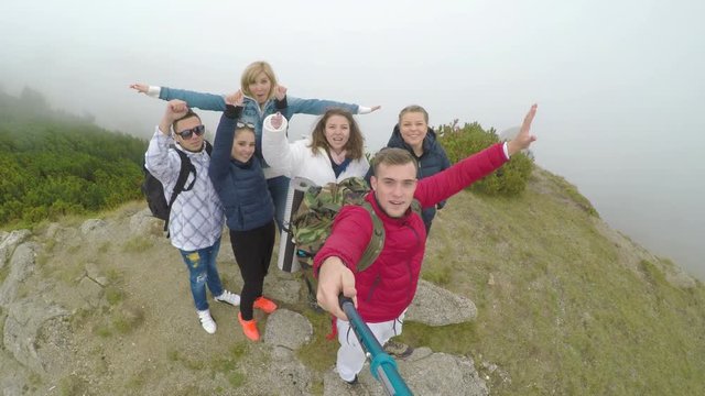Group of teenage cheering friends having a video selfie chat standing on top of mountain sharing their trip adventure 