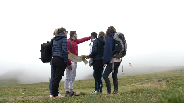 Lost group of teenage friends checking the map trying to find out the right way on foggy mountain top