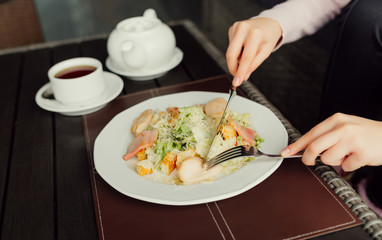 Lunch at restaurant. Female hands using fork and knife for caesar salad. Close-up view.