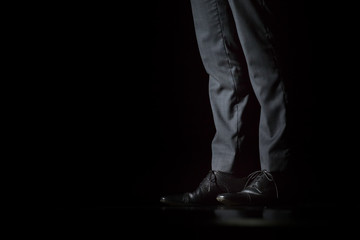 Fototapeta na wymiar Young fashion businessman's legs in classic pants and shoes on black background.