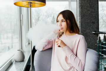 Vaping. Young beautiful girl smoking ( vaping ) e-cigarette with smoke in restaurant. Vapor concept.