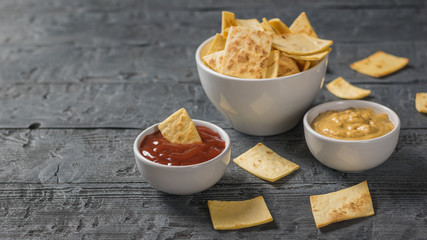 Mexican tortilla chips in a bowl with sauce and mustard on the dark table.