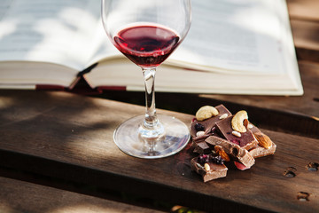 Glass with wine and pieces of chocolate near open book