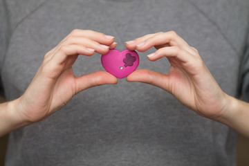 woman hands holding pink heart on gray background