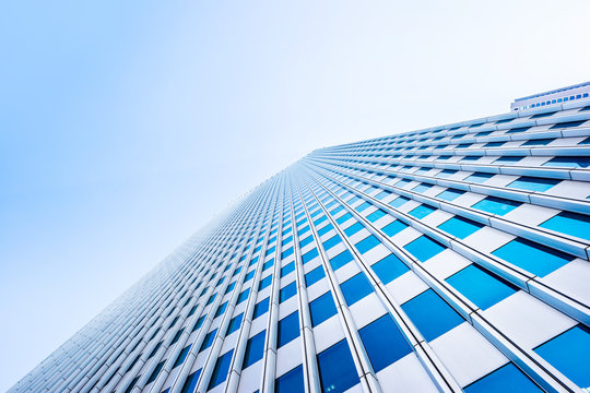 Asia Business concept for real estate and corporate construction - looking up view in financial district, the silhouettes of skyscrapers reflect blue sky in Tokyo, Japan.
