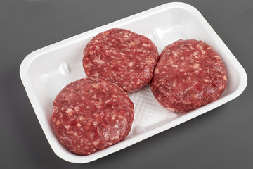 Tray with raw beef burgers isolated on gray background