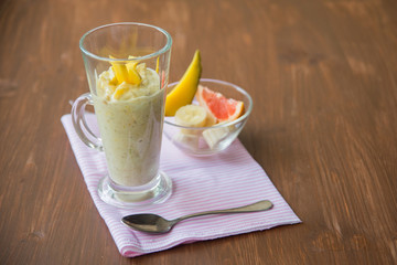 fresh smoothies in glass glass with banana, orange, mango, on wooden background.