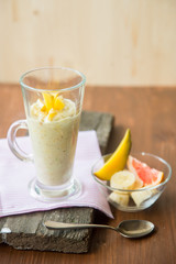 fresh smoothies in glass glass with banana, orange, mango, on wooden background.