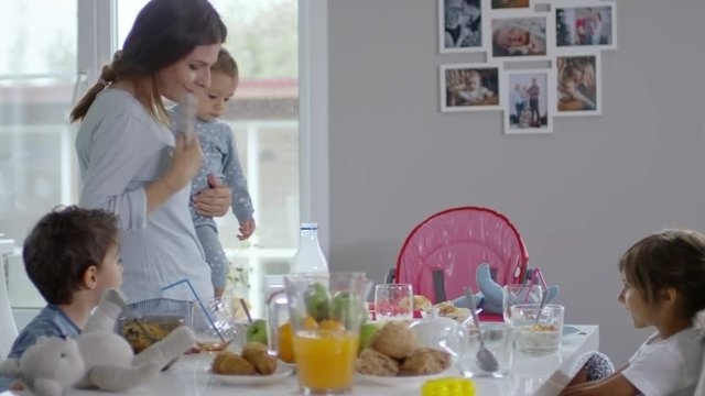 Mother carrying a baby and pouring milk into bottle while talking on the phone
