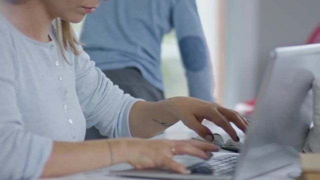 Mother sitting at desk and working on laptop computer while her son of preschool age stops drawing and goes to do something else