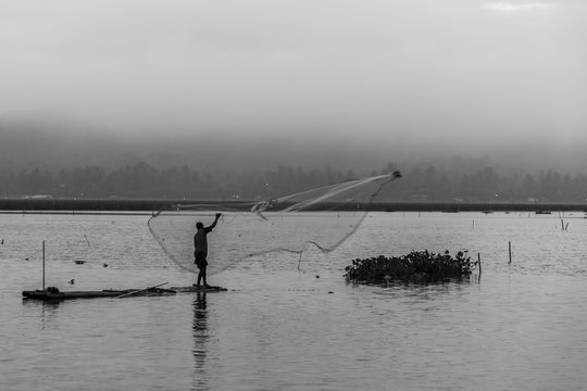 Black and white photo of fisherman in foggy misty morning.