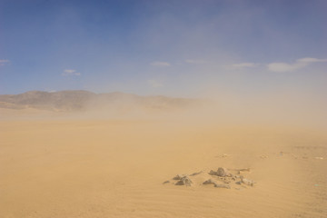 Clouds of sand blow around rocks in the midst of a vast sand desert.