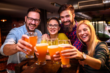 Group of young friends in bar drinking beer toasting