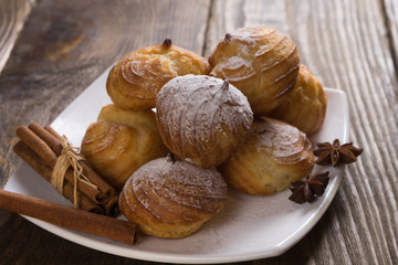 Delicious eclairs sprinkled with icing sugar, stand on a wooden table. Copy spase.