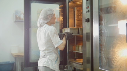 Female bakes on commercial kitchen - woman puts baking in the oven