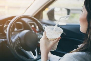 Asian woman holding iced coffee cup drinking while driving, cold tone added soft light effect