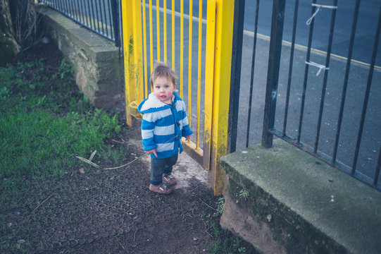 Little boy standing by the gate of a playground