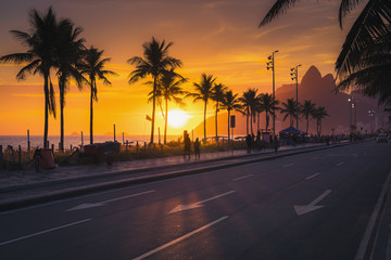 Sunset over Ipanema Beach with Dois Irmaos mountains in Rio de Janeiro, Brazil. People walking by...
