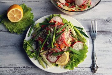Spring vegetables salad on the white plate. Radish, tomato, celery and cucumber. Topped with sesame seeds. Vegetarian dish on the white wooden table. Top view.