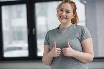 Obese girl showing thumbs up in gym