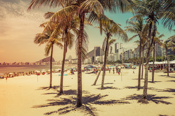 Copacabana Beach full of people view through coconut palms in Rio de Janeiro, Brazil. Light effect...