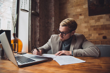 Young busy man is signing papers and working on the laptop.