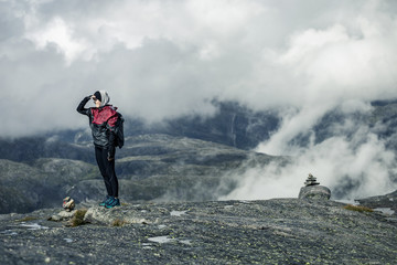 Silhouette of young woman in raincoat walking along the plateau through the foggy place on the way...