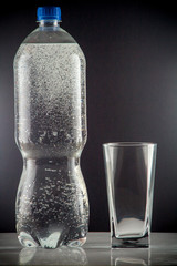 Pure mineral water pouring from a bottle into a glass. bottle of clear drinking cold mineral water with gas in isolation on the background next to a glass transparent glass
