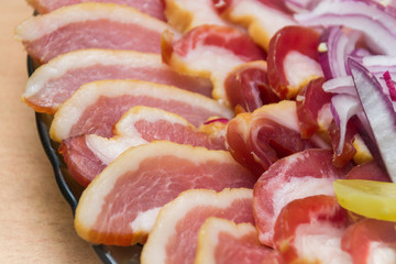 Close-up of ham, bacon, lettuce, cucumber and onion on paper, on a platter