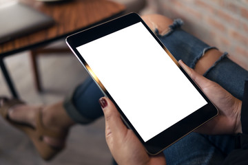 wearing ripped jean sitting cross legged , holding black tablet pc with blank white desktop screen on thigh in cafe