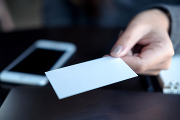 Business woman holding and giving business card to someone with mobile phone and notebook on table in office