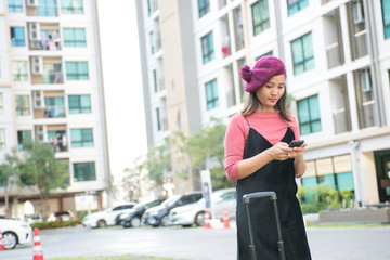 Naklejka premium travel, business trip, people and technology concept - happy Young woman with travel bag and and talking on smartphone on city street
