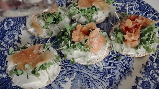 Putting pepper on healthy oatcake canapes with sprouts and white cheese. Hand picks up one sandwith from a blue plate