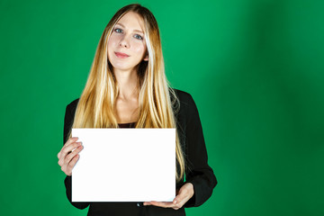 Attractive blonde business woman holding white banner with copy space for additional text or graphic. Girl is posing on a green background. Positive emotions