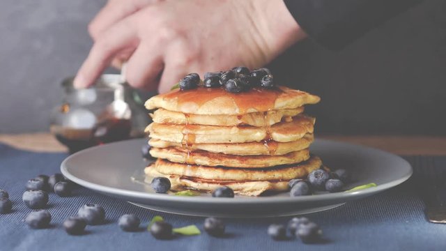 best american pancake with blueberries and syrup - hand adding honey