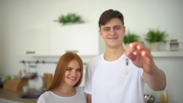 Young Couple Holding New House Keys. Close up shot of young couple hands holding key from their new stylish home on the living room kitchen background. Key to a new home. Happy couple in love holding