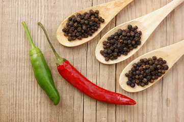 Black and red pepper in wooden spoon on the old board