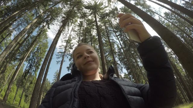 Cute millennial woman relaxing in a forest using smartphone mobile for selfie photo shooting