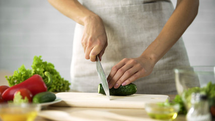 Female chef slicing fresh cucumber with a knife on wooden board, vegetables