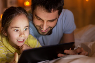 family with tablet pc in bed at night at home