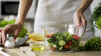 Obraz na płótnie Canvas Housewife taking saltshaker on table for seasoning lunch salad, tasty appetizer