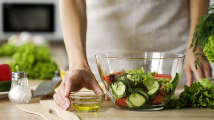 Young wife holding olive oil dressing bowl for seasoning fresh salad, dieting
