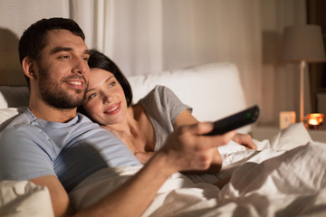 happy couple watching tv in bed at night at home